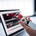 hand holding a phone with screen on a news site in front of  a laptop on a news web page